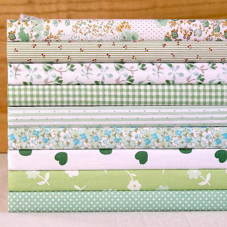 May include: A stack of ten fabric squares in various green and white patterns. The patterns include floral, gingham, polka dot, and stripes.
