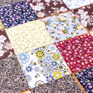 Pode incluir: Um edredom de patchwork com uma variedade de quadrados de tecido estampados com flores e padr&otilde;es. Os quadrados s&atilde;o em tons de azul, vermelho, amarelo e castanho, com desenhos florais e paisley. O edredom &eacute; provavelmente feito &agrave; m&atilde;o.
