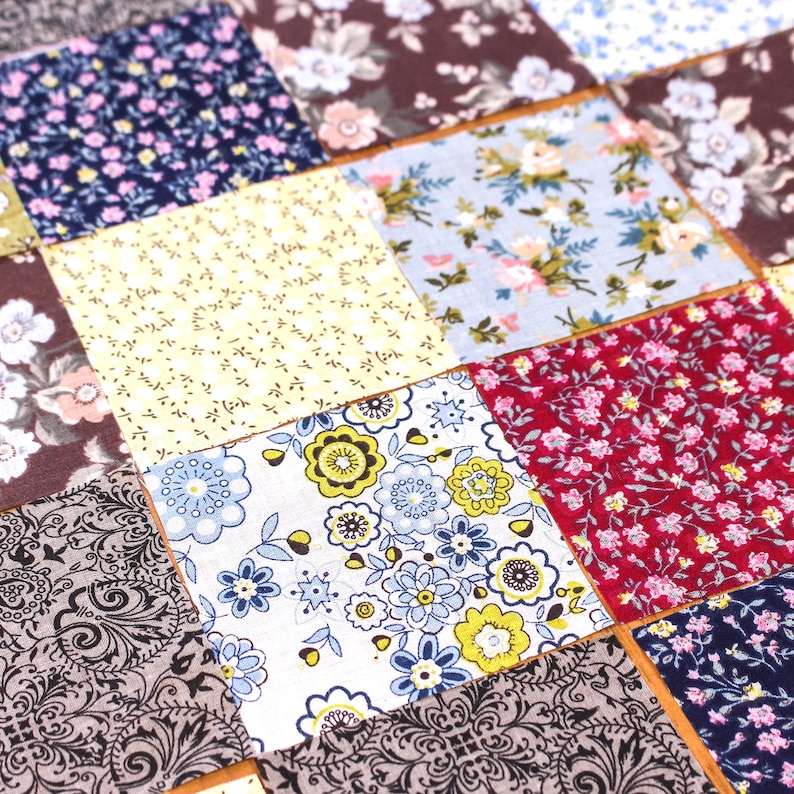 Pode incluir: Um edredom de patchwork com uma variedade de quadrados de tecido estampados com flores e padr&otilde;es. Os quadrados s&atilde;o em tons de azul, vermelho, amarelo e castanho, com desenhos florais e paisley. O edredom &eacute; provavelmente feito &agrave; m&atilde;o.