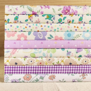May include: A stack of 10 fabric squares with various floral patterns in shades of pink, purple, and white. The fabric squares are arranged in a vertical stack.