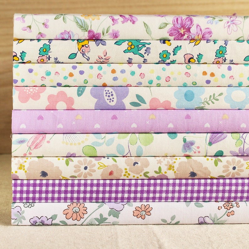 May include: A stack of 10 fabric squares with various floral patterns in shades of pink, purple, and white. The fabric squares are arranged in a vertical stack.
