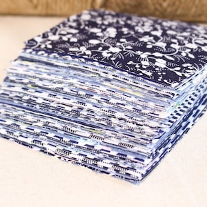 May include: A stack of fabric squares in various blue and white patterns. The top square has a floral design.