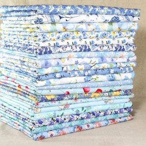 May include: A pile of folded fabric, predominantly blue and white, with floral designs. The patterns vary, including small and large flowers, leaves, and other botanical motifs. The fabrics are neatly stacked, displaying a range of patterns and shades of blue.