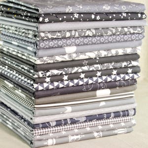 Puede incluir: Una pila de cuadrados de tela doblados en varios tonos de gris y blanco. Las telas presentan diversos patrones, incluyendo diseños florales, geométricos y abstractos. Las telas están cuidadosamente apiladas, mostrando una variedad de texturas y estilos.