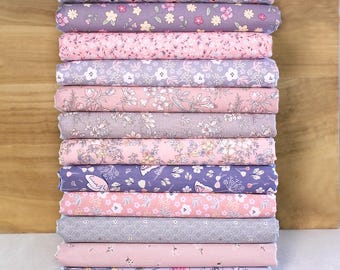 May include: A stack of floral fabric rolls in various pastel colors, including pink, purple, and gray. Each roll displays a different floral pattern, creating a visually appealing display. The fabric is likely cotton or a similar material, suitable for quilting or sewing projects.