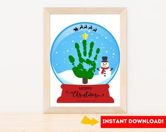 May include: Framed Christmas art print featuring a snow globe design. Inside the globe, a green handprint tree, a snowman, and falling snow are visible. The words "Merry Christmas" are written on a red banner below the globe. The image is framed in a light wood frame.