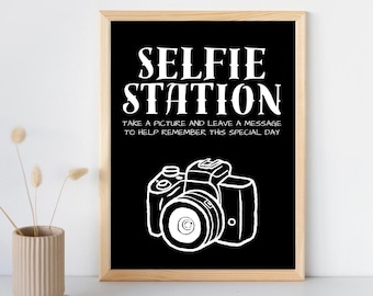 May include: Black and white sign with the text "SELFIE STATION" and the words "TAKE A PICTURE AND LEAVE A MESSAGE TO HELP REMEMBER THIS SPECIAL DAY". A white outline of a camera is below the text.