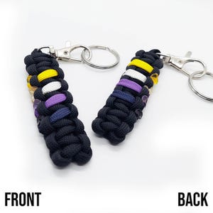 May include: A black paracord keychain with a yellow, white, purple, and blue color pattern. The keychain has a silver metal key ring.
