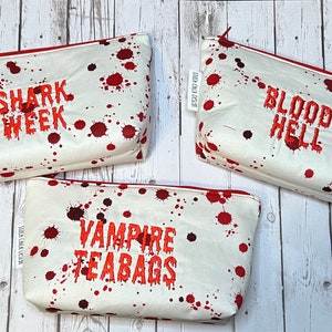 Op de afbeelding: Drie witte ritszakjes met rode bloedspatten. De zakjes hebben de volgende tekst: "Shark Week", "Bloody Hell" en "Vampire Teabags".