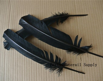 May include: Three black feathers with a natural quill and fluffy tips. The feathers are arranged in a fan shape on a brown surface.