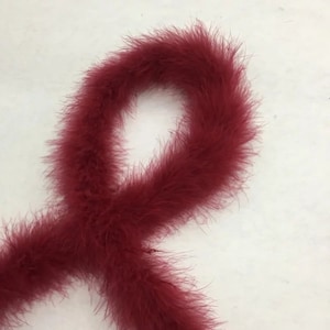 Pode incluir: Um longo boa de penas de cor bordô. O boa é feito de penas macias e fofas e é perfeito para adicionar um toque de glamour a qualquer roupa.