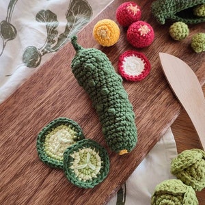 May include: A wooden cutting board with a green crocheted cucumber, cucumber slices, red and yellow crocheted tomatoes, and a wooden spoon.