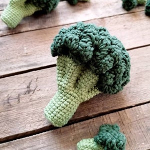 May include: A collection of crocheted broccoli, ranging in size, with a green and light green color scheme. The broccoli is displayed on a wooden surface.