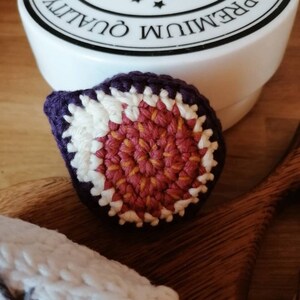 May include: Two crocheted fig ornaments, one with a purple, white, and orange design and the other with a white base and gray stars.