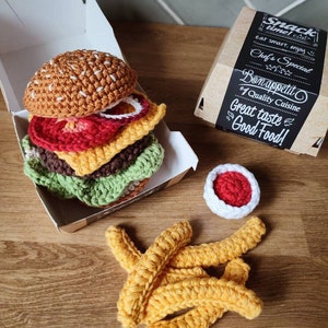 May include: Crocheted hamburger, french fries, and a small bowl of ketchup in a brown paper box. The box has a black label with the text "Snack time! Eat smart, enjoy. Chef's Special. Bon appetit. #1 Quality Cuisine. Great taste! Good Food!"