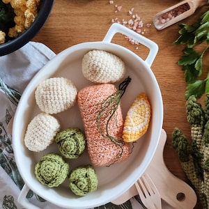 Puede incluir: Un plato de cerámica blanco lleno de alimentos de ganchillo, incluyendo un filete de salmón, una rodaja de limón, coles de Bruselas y coliflor. El plato está sobre un mantel estampado blanco y verde.