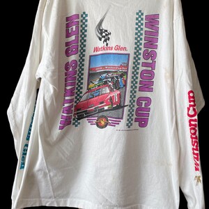 May include: White long-sleeve t-shirt with a graphic of a race car on a track at Watkins Glen. The text "Watkins Glen" and "Winston Cup" are printed on the shirt.