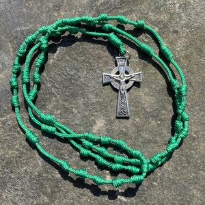 May include: A green knotted rosary with a silver Celtic cross pendant. The rosary is made of braided cord with knots at regular intervals.