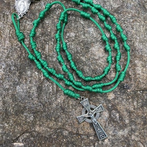 May include: Green knotted rosary with a silver Celtic cross and a silver medal of the Virgin Mary.