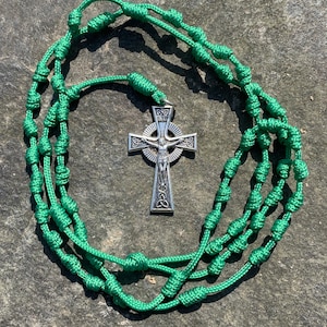 May include: Green knotted rosary with a silver Celtic cross pendant. The cross features a depiction of Jesus Christ.