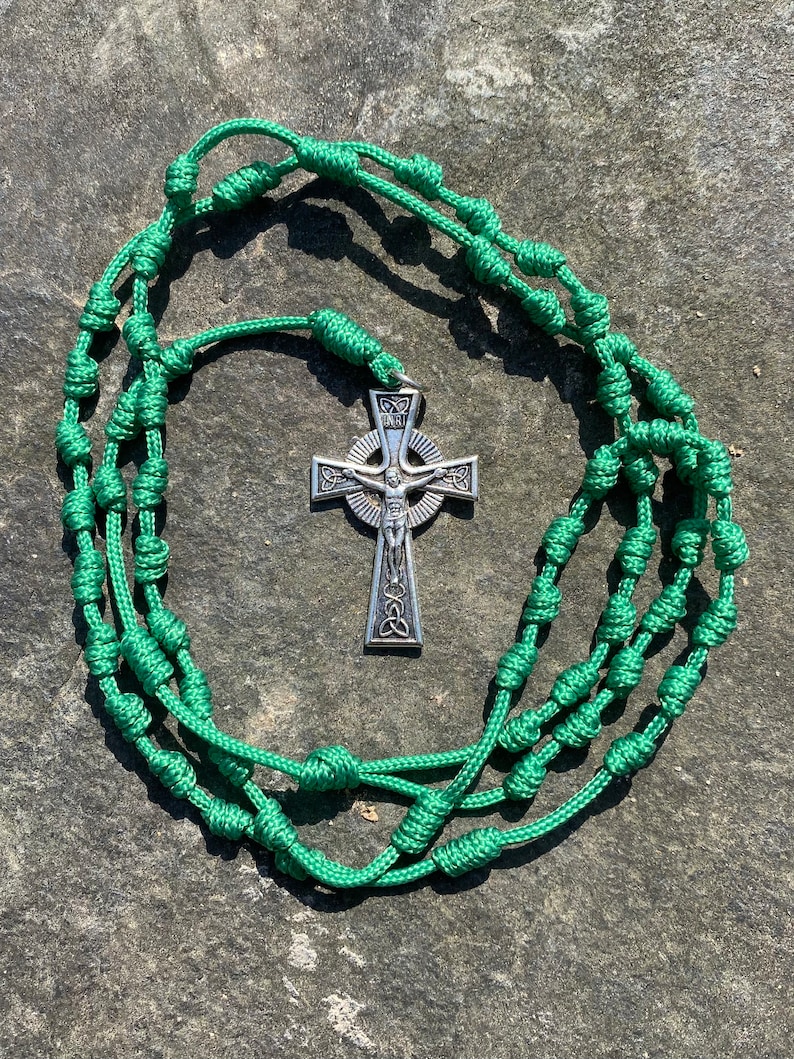 May include: Green knotted rosary with a silver Celtic cross pendant. The cross features a depiction of Jesus Christ.