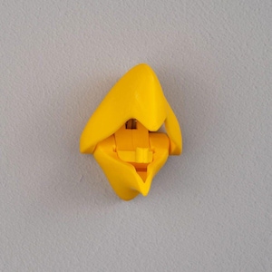 Peut inclure: Un objet en plastique jaune vif avec une forme abstraite unique. L'objet semble être une conception pliée ou articulée, avec une section centrale et des extensions incurvées en forme de pétales. La forme générale est symétrique et accrocheuse, sur fond gris neutre.