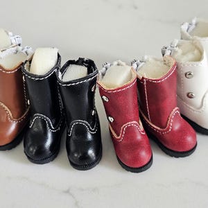 May include: A collection of miniature boots in various colors, including brown, black, red, and white. Each boot features a faux fur lining and decorative stitching. The boots are designed for dolls or other small figures.