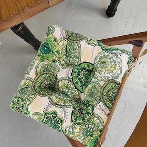 May include: A white and green patterned chair cushion with a mandala design. The cushion is made of a soft, plush fabric and is perfect for adding a touch of style to any chair.