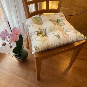 Peut inclure: Une chaise en bois avec un coussin blanc orné d'un motif de branche d'olivier verte et du texte "Olive Oil".