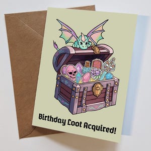 May include: Greeting card with a cartoon illustration of a treasure chest filled with gems, potions, and a skull. A small dragon sits atop the chest. The text "Birthday Loot Acquired!" is at the bottom of the card. Includes a brown envelope.