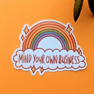 May include: A sticker with a rainbow and a cloud that says "MIND YOUR OWN BUSINESS". The rainbow has orange, red, yellow, green, blue, and purple stripes. The cloud is white with a brown outline.