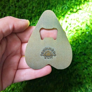 Puede incluir: Un abridor de botellas en forma de coraz&oacute;n de color dorado con un dise&ntilde;o recortado y las palabras "Casmere Sun" impresas en &eacute;l.