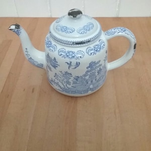 May include: A white enamel teapot with a blue and white floral pattern. The teapot has a spout and a handle.