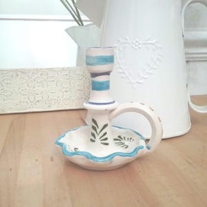 May include: White ceramic candle holder with a blue and green striped design and a handle. The holder has a scalloped edge and a small, round base.