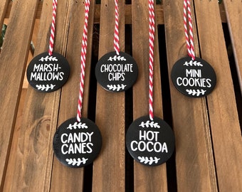 May include: Five black round gift tags with white text and red and white twine. The tags read "Marshmallows", "Chocolate Chips", "Mini Cookies", "Candy Canes", and "Hot Cocoa".