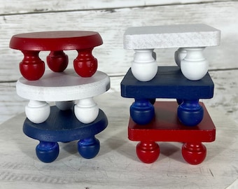 May include: Three tiered wooden candle stands painted in red, white, and blue. The stands are stacked on top of each other, creating a patriotic display.