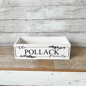 May include: White wooden box with black lettering that reads "The Pollack Family" with leafy accents.