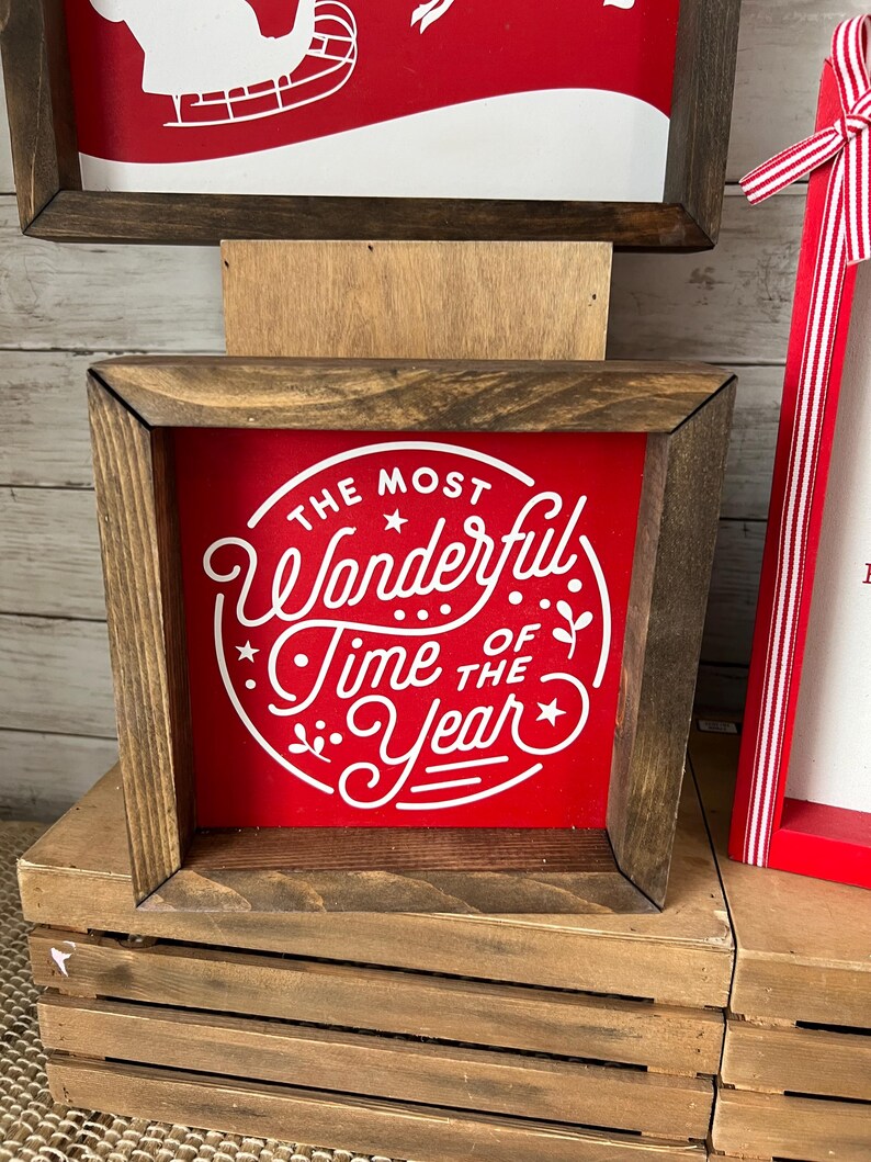 May include: A wooden framed sign with a red background and white text that reads "The Most Wonderful Time of the Year".