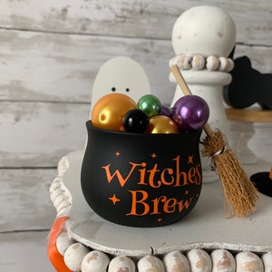 May include: Black cauldron with orange "Witches Brew" text and stars, filled with colorful beads and a small broom.