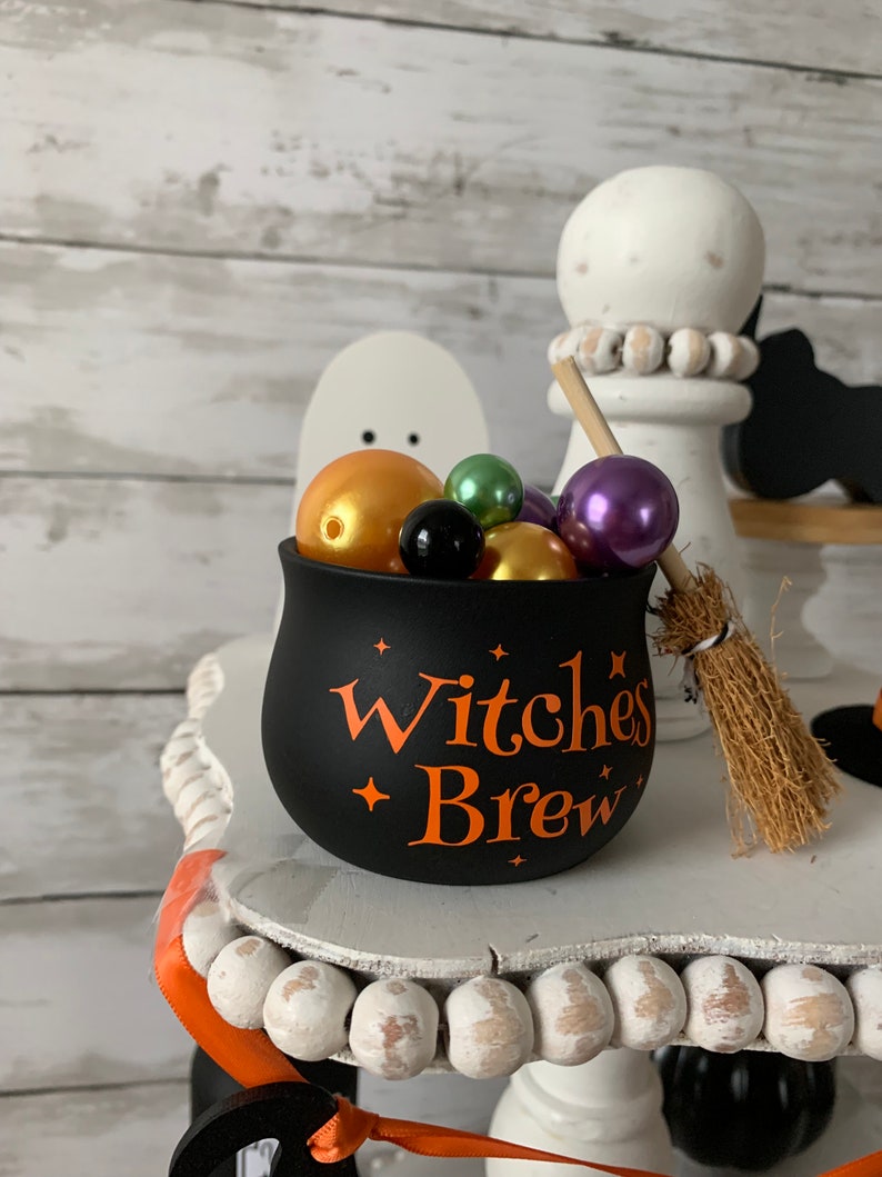 May include: Black cauldron with orange "Witches Brew" text and stars, filled with colorful beads and a small broom.