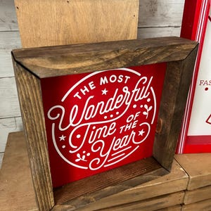 May include: A wooden framed sign with a red background and white lettering that reads "The Most Wonderful Time of the Year".