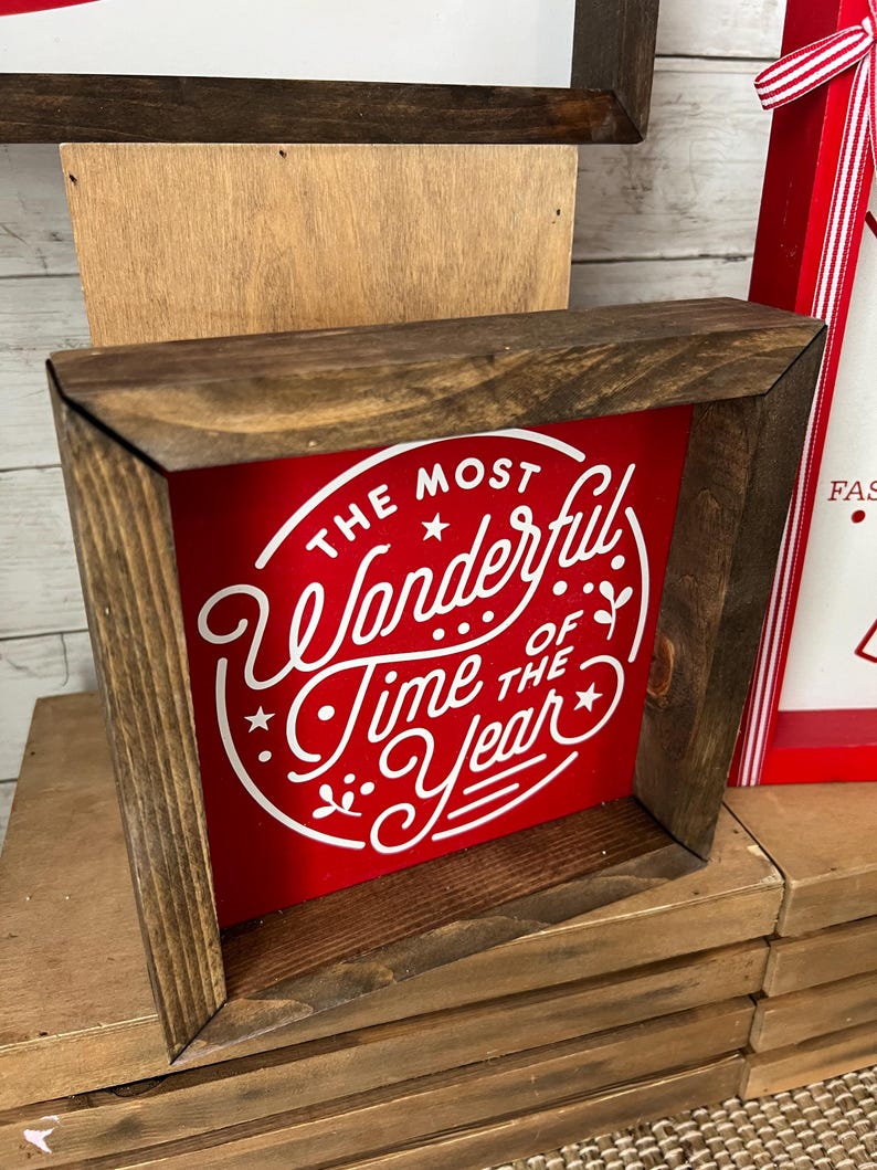 May include: A wooden framed sign with a red background and white lettering that reads "The Most Wonderful Time of the Year".