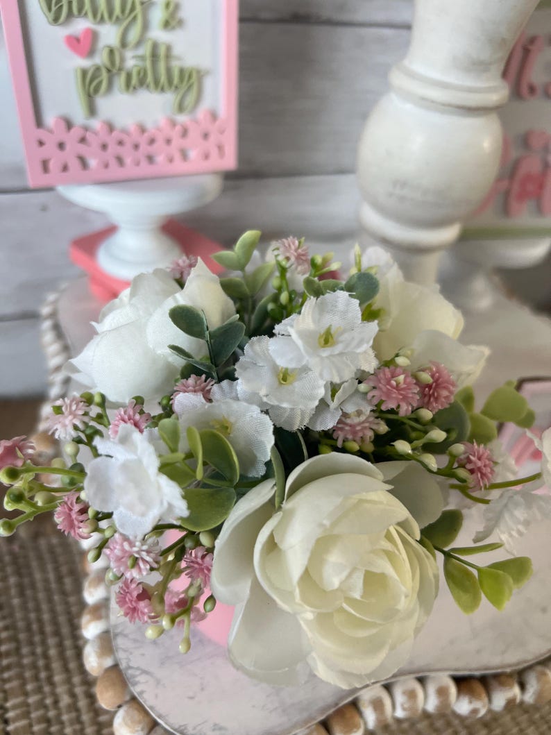 May include: A small pink planter with a bouquet of white and pink flowers. The flowers include white roses, small white flowers, and pink buds.