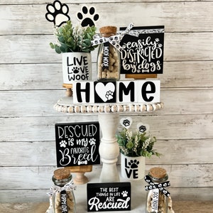 May include: A tiered white tray with black and white dog-themed decor. The top tier features a small potted plant, a glass jar filled with dog treats, and a sign that reads "easily distracted by dogs". The middle tier features a sign that reads "HOME" and a sign that reads "rescued is my favorite breed". The bottom tier features a sign that reads "the best things in life are rescued", a glass jar filled with dog treats, and a small potted plant with a sign that reads "love".