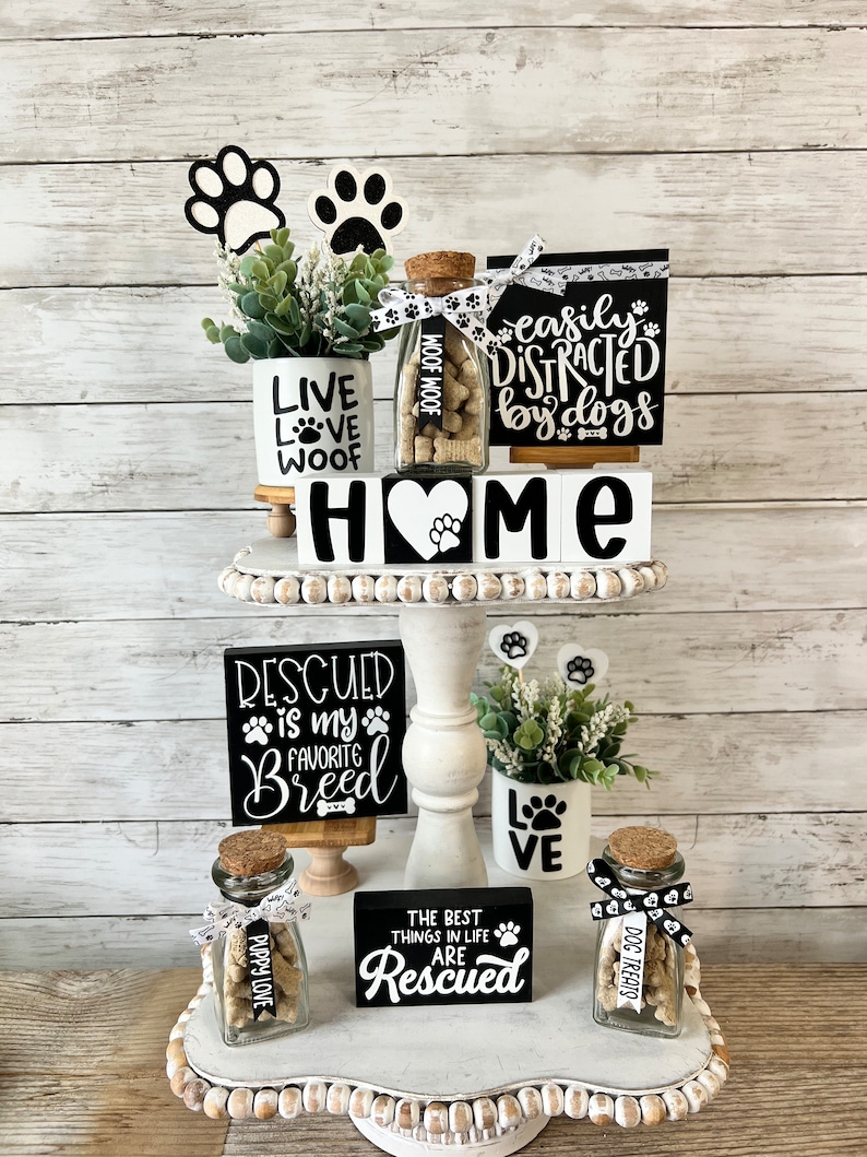 May include: A tiered white tray with black and white dog-themed decor. The top tier features a small potted plant, a glass jar filled with dog treats, and a sign that reads "easily distracted by dogs". The middle tier features a sign that reads "HOME" and a sign that reads "rescued is my favorite breed". The bottom tier features a sign that reads "the best things in life are rescued", a glass jar filled with dog treats, and a small potted plant with a sign that reads "love".
