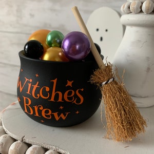 May include: Black cauldron with the text "Witches Brew" in orange lettering, filled with colorful beads and a small brown broom.