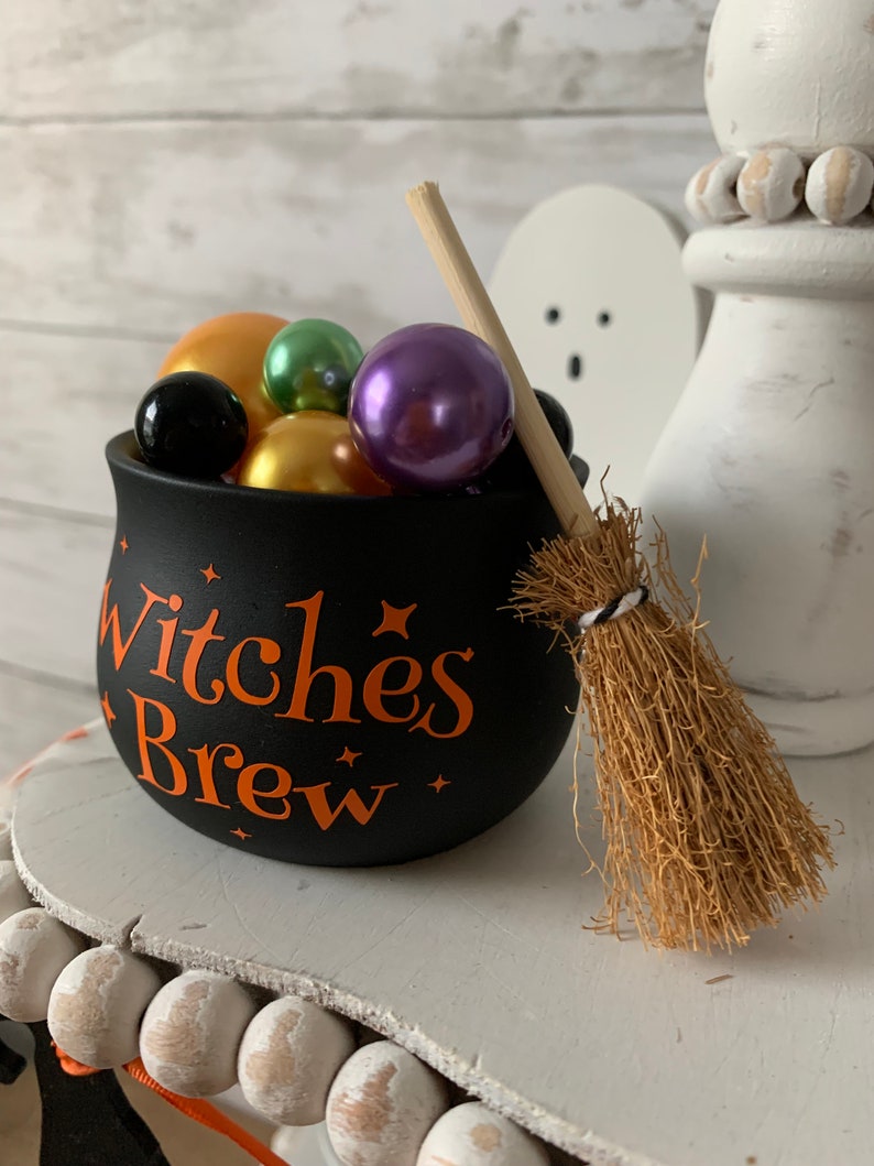 May include: Black cauldron with the text "Witches Brew" in orange lettering, filled with colorful beads and a small brown broom.
