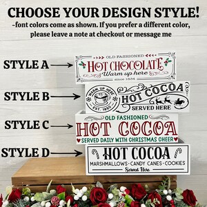 May include: Four different styles of white wooden signs with red, green, and black lettering. The signs advertise "Hot Cocoa" with different variations of the text and graphics. The signs are stacked on top of each other.