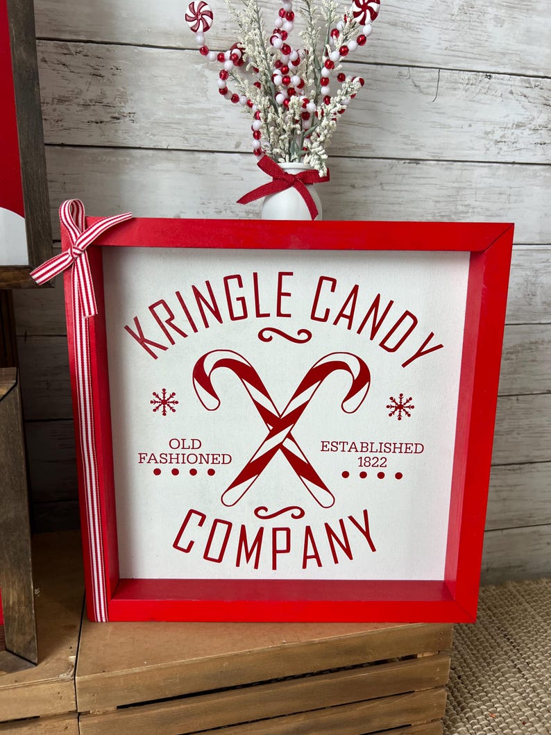 May include: Red wooden framed sign with white background and red text that reads "Kringle Candy Company" with a red candy cane graphic and the text "Old Fashioned" and "Established 1822".