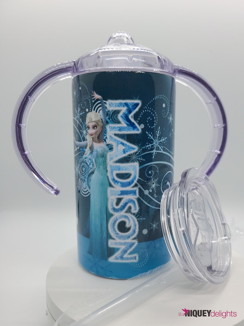 K&ouml;nnte beinhalten: Ein blau-wei&szlig;er Trinkbecher mit der Figur Elsa aus dem Film Frozen, mit dem Namen "MADISON" in Wei&szlig;. Der Becher hat lila Griffe, einen transparenten Deckel und Strohhalm. Der Becher ist mit Schneeflocken verziert.
